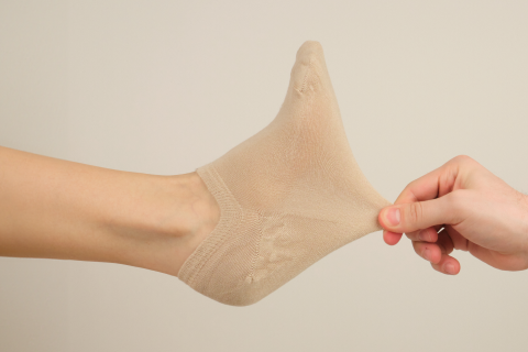 A hand stretches a light beige Hugh Ugoli sock to show its flexibility and snug fit.