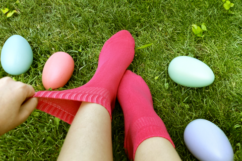 Bright pink socks in a lush green setting with colorful Easter eggs, portraying a fun and festive holiday atmosphere.