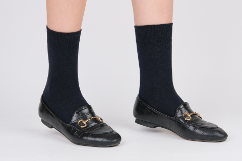 A close-up view of feet clad in navy blue Hugh Ugoli socks, paired with classic black loafers featuring gold buckles, presenting a sleek and sophisticated style.