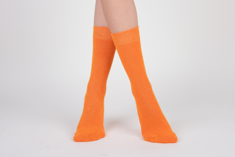 Bright orange Hugh Ugoli socks worn up to the calf, adding a pop of color against a white backdrop.