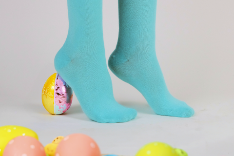 A pair of light turquoise socks stands amidst a playful scatter of colorful Easter eggs, highlighting a festive spirit and springtime freshness.