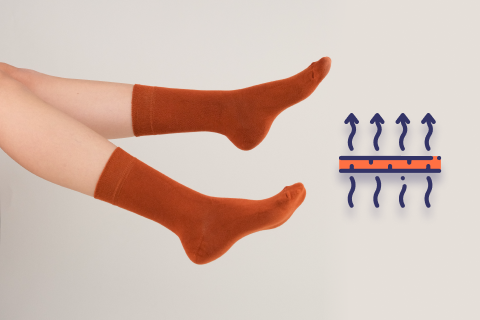 A pair of legs elevated and crossed at the ankles, showcasing terracotta-colored socks. To the right, a symbol illustrates the socks' breathable feature, with arrows indicating airflow through the fabric.