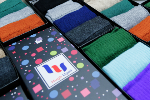 Assortment of Hugh Ugoli socks in various colors presented in a box with a logo-branded lid.