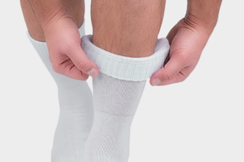 Close-up of hands pulling up white crew socks on legs, with a focus on the ribbed texture around the calf area.