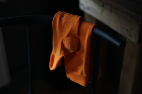A burnt orange Hugh Ugoli sock casually hanging over a chair's armrest, set against a dark, moody background.