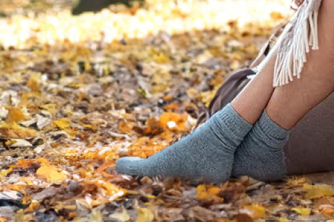 A person seated amidst autumn leaves, wearing Hugh Ugoli's heather blue socks, capturing the essence of fall comfort.