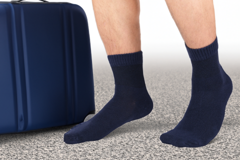 A traveler standing in dark blue socks beside a blue suitcase, ready for a journey, showcasing the practicality and style of travel-friendly socks.