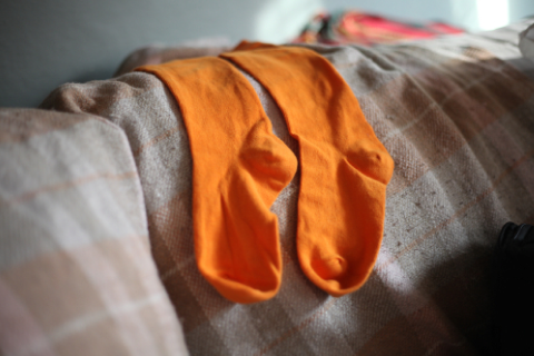 A pair of bright orange socks laid out on a beige patterned couch.