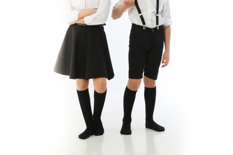 Two children in school uniforms, one in a skirt and the other in shorts, both wearing black Hugh Ugoli knee-high socks, ready for a school day.
