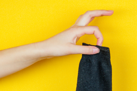 Hand holding a black sock against a vibrant yellow background, emphasizing the feel and fabric quality of Hugh Ugoli socks.