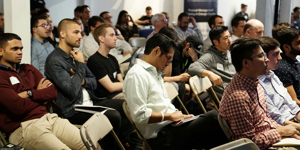 Picture shows a number of people sat in a tech conference looking forward to the speaker.