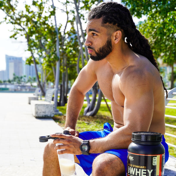 Man sitting on a park bench with whey protein shaker bottle