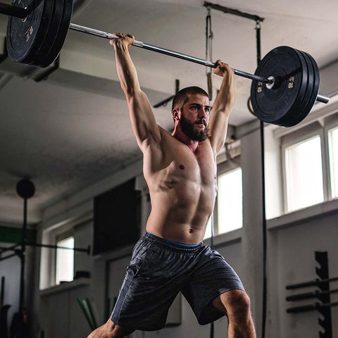 Man lifting weighted barbell above head in the gym as part of bodybuilding workout