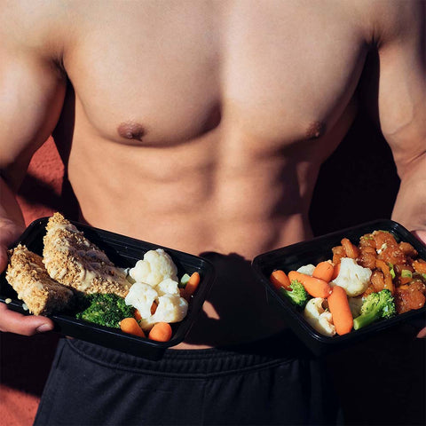 Shirtless bodybuilder holding out packed meals as part of meal prep for bodybuilding workout regime.