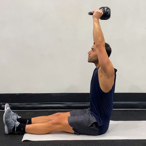 Man sitting on exercise an matt holding a kettlebell