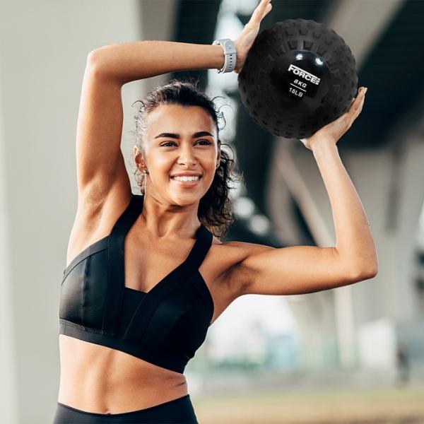 Lady lifting a Force USA Slam Ball outdoors above her head