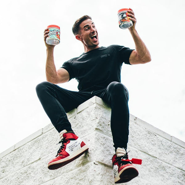 Man sitting on ledge holding a tub of Ghost Pre-workout