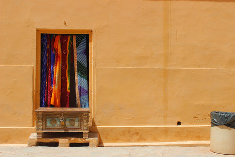 Colourful handloom fabrics displayed through a rural house window