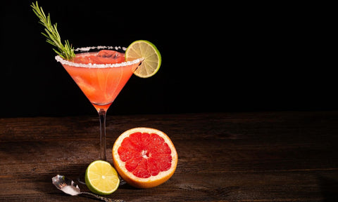 zero proof cocktail in a martini glass with half a grapefruit and sprig of rosemary for garnish