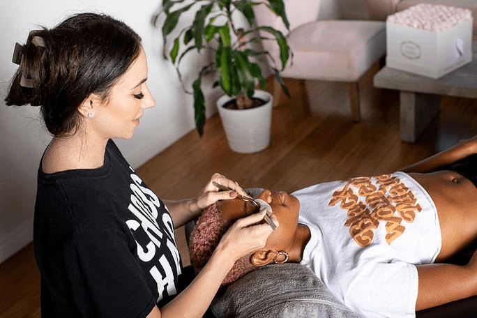 A smiling woman performing lash extensions on a client