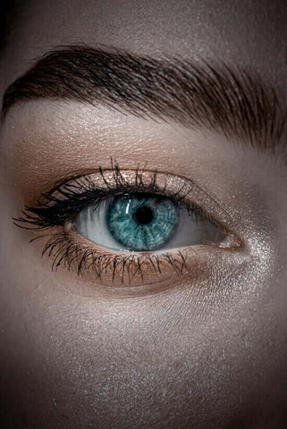 a woman’s blue eye with lash extensions and gold eyeshadow