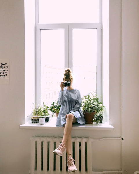 a woman taking a photo in front of a sunny window