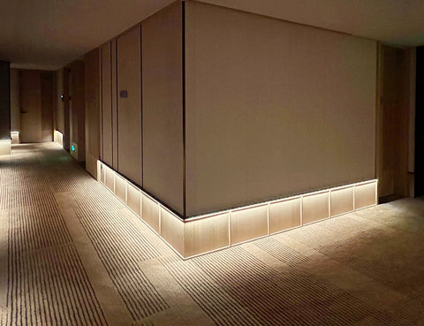 The application of angle recessed aluminum channels produces a soft ambient light that fosters a welcoming and serene atmosphere in a hotel corridor.