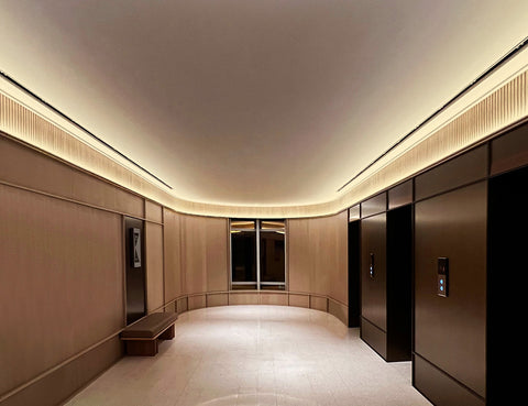 The application of angle recessed aluminum channels produces a soft and inviting ambient light that fosters a welcoming and serene atmosphere in a hotel elevator lobby.