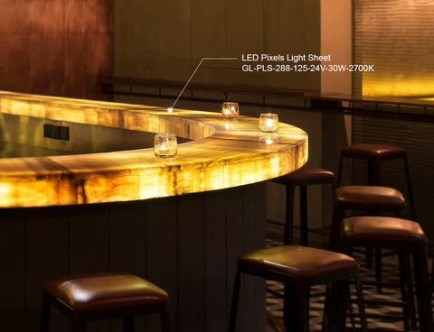 Warmly lit bar counter with LED Pixels Light Sheet lighting, model GL-PLS-288-125-24V-30W-2700K, showcasing a glossy finish on natural wood and leather-topped bar stools in an elegant setting.