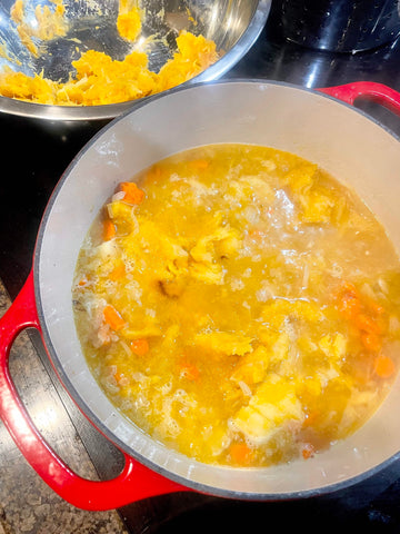 Dutch oven on a stove with chicken stock, veggies, and pumpkin meat