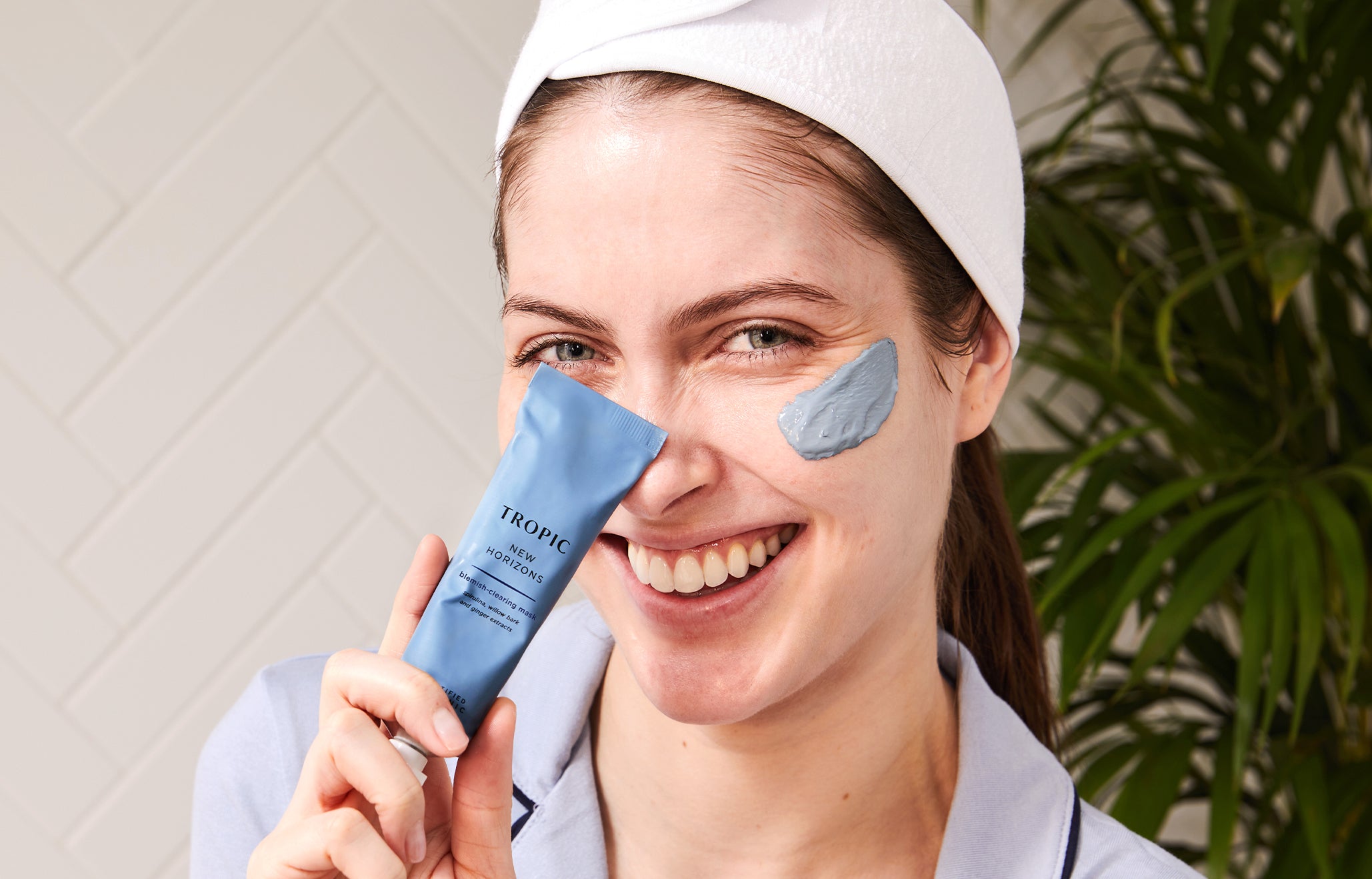 model holding new horizons blemish-clearing mask to face with product applied to her cheekbone