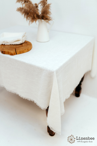 White linen tablecloth with frayed edges is on an antique table