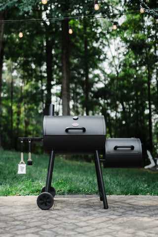 A closed Smokin' Pro Grill and Offset Smoker sitting on a paved patio in front of a line of trees