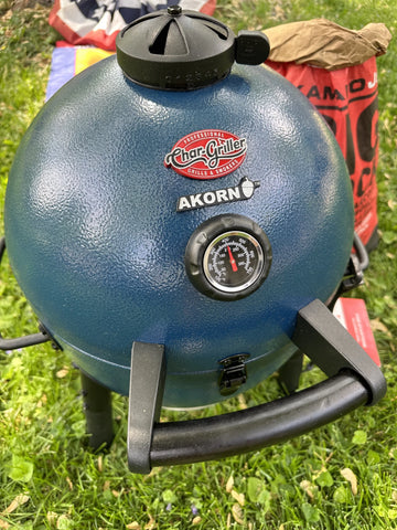 A blue AKORN Jr. grill sitting on grass in front of a bag of Kamado Joe Big Block XL Lump charcoal