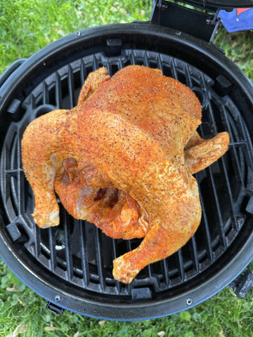 A seasoned whole chicken sits on the cooking grate of an open AKORN Jr. kamado grill