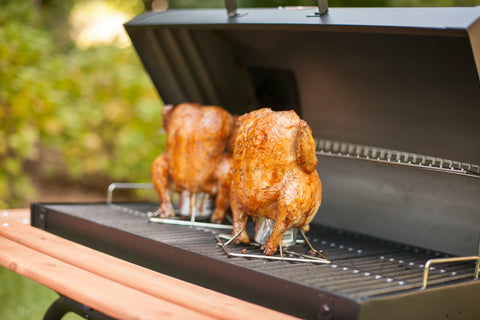 2 whole chickens on chicken stands roast on an open barrel grill