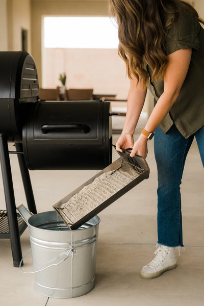 Susie from Hey Grill Hey empties the ash tray from a Char-Griller grill into a metal bucket