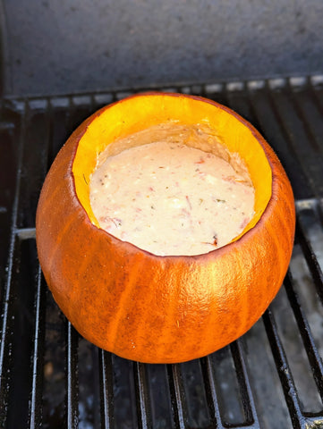 A pumpkin full of queso dip sits on a grill grate