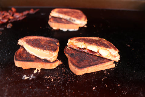 Closeup of 3 grilled cheese sandwiches cut in half diagonally, with the half away from the camera propped up on the half towards the camera showing the fillings