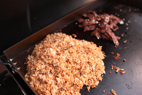 A mound of fried rice (foreground) and a mound of Korean BBQ strips (rear) on the cooking surface of a Flat Iron Gas Griddle