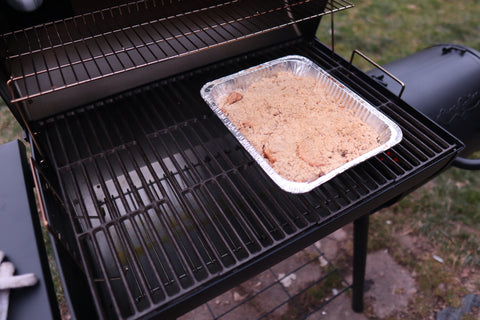 An aluminum tray filled with apple crisp sits on the cooking grate of a grill ready to cook