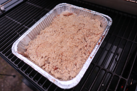 Closeup of a tray of apple crisp on the cooking grate of a grill, ready for smoking