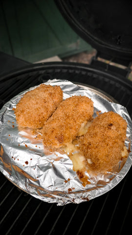 3 cordon bleu rolls on a foil-lined baking sheet on the cooking grate of an Auto-Kamado grill. Melted cheese oozes from the rolls.