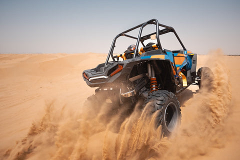 A blue and orange UTV drives through sandy terrain, showcasing accessories during spring break