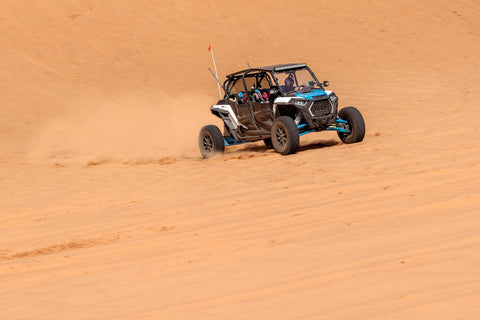 A person driving a UTV on sand dunes with safety glass rear windows
