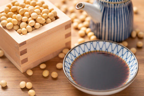 A small bowl of koikuchi shoyu next to soybeans