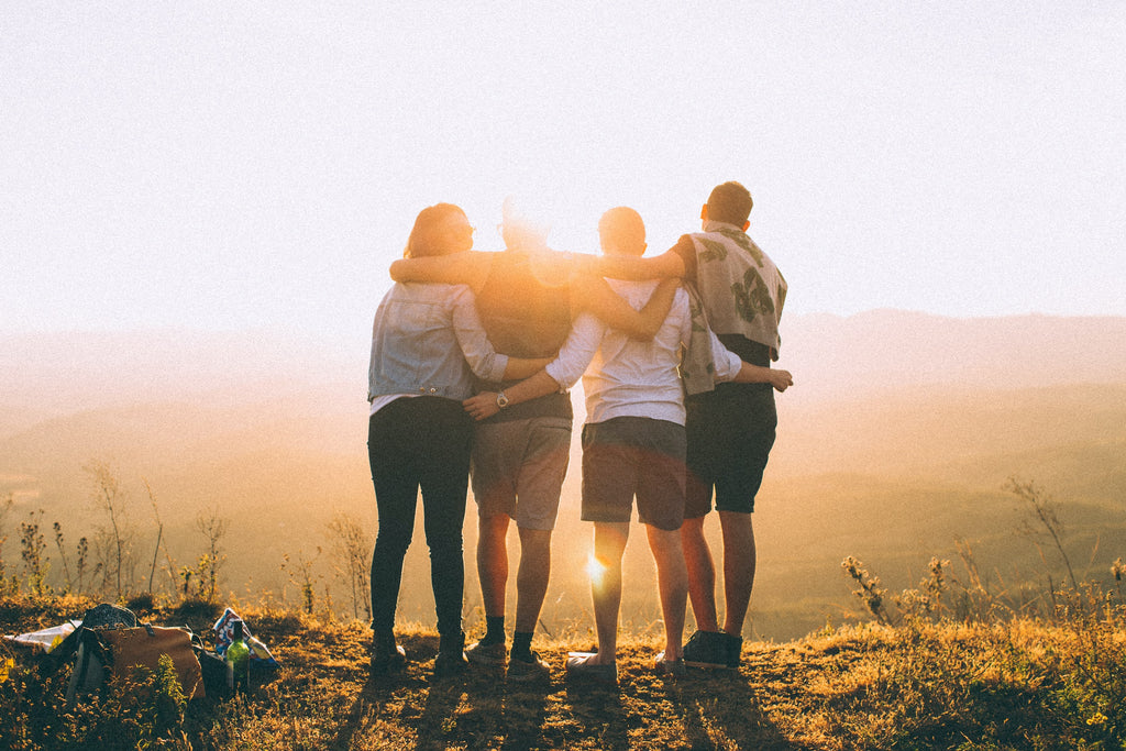 Four person group with hands wrapped around each other while looking at sunrise