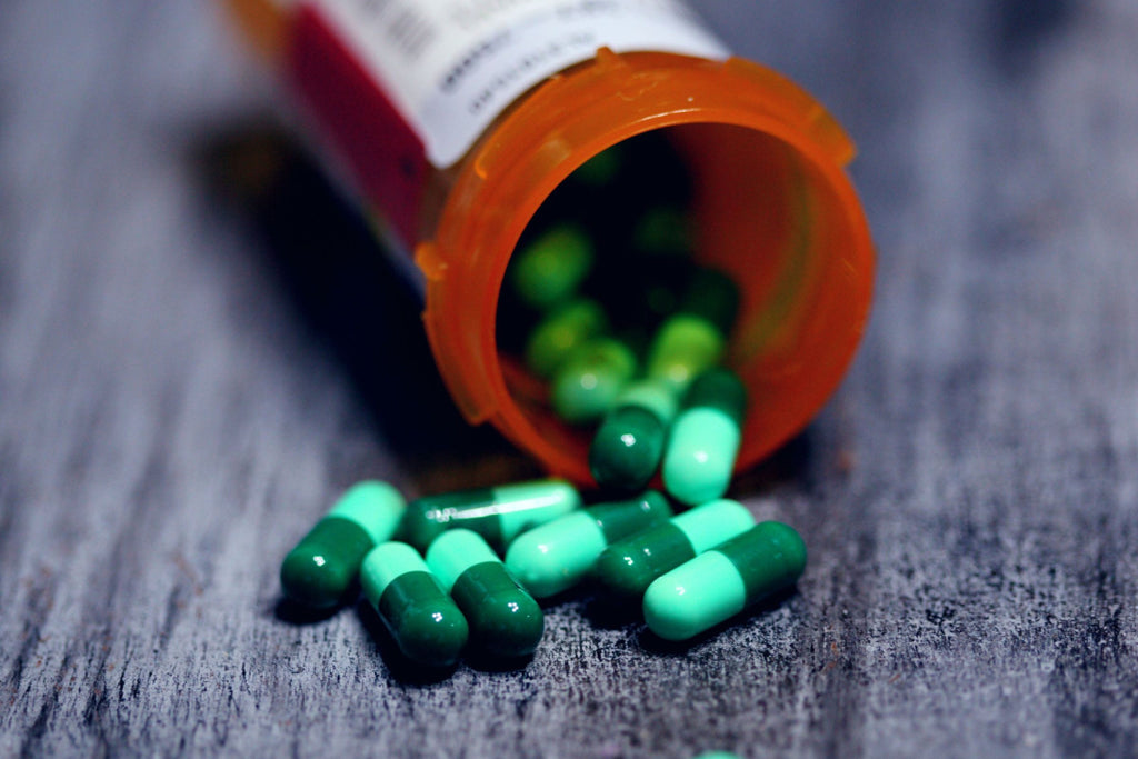 Prescription bottle spilling green capsules on a wooden surface