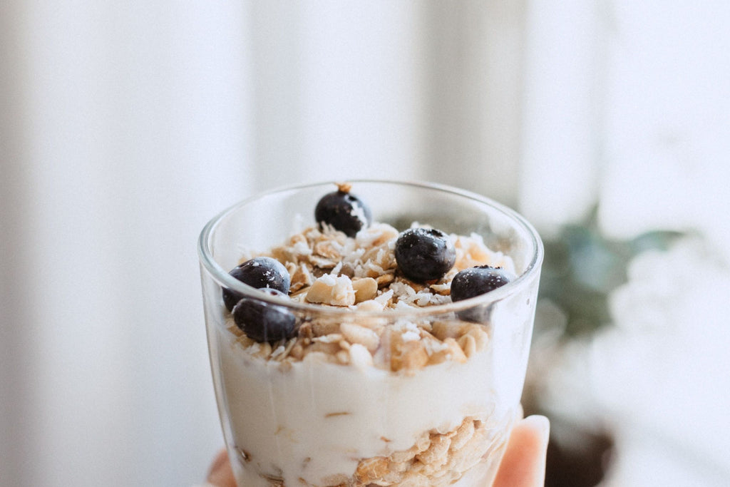 hand holding glass bowl of oatmeal, yoghurt and blueberries