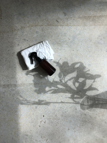 Photo of amber spray bottle lying on floor in the shadow of beautiful flowers